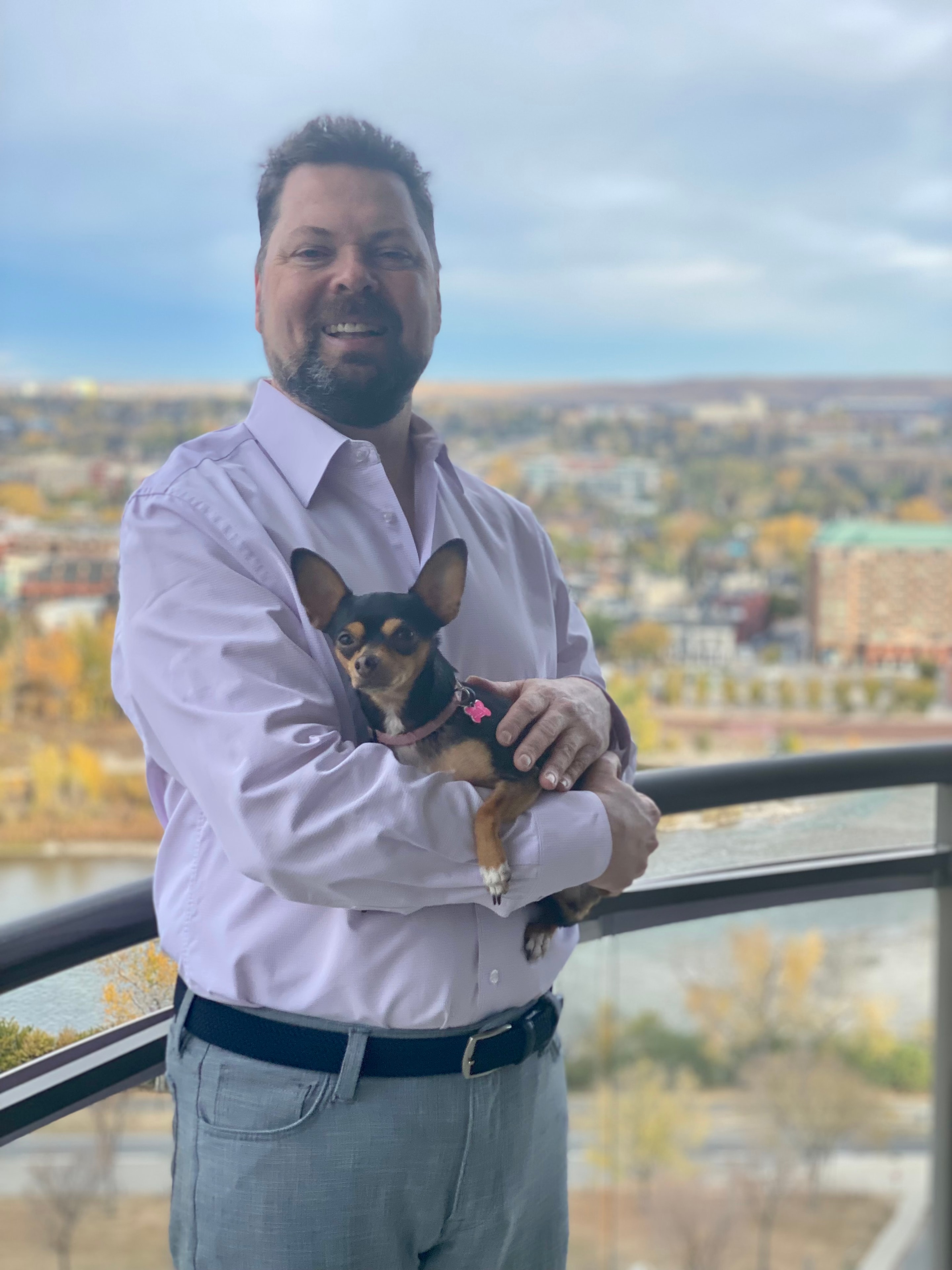 Ken Engler holding his dog on a balcony overlooking the city
